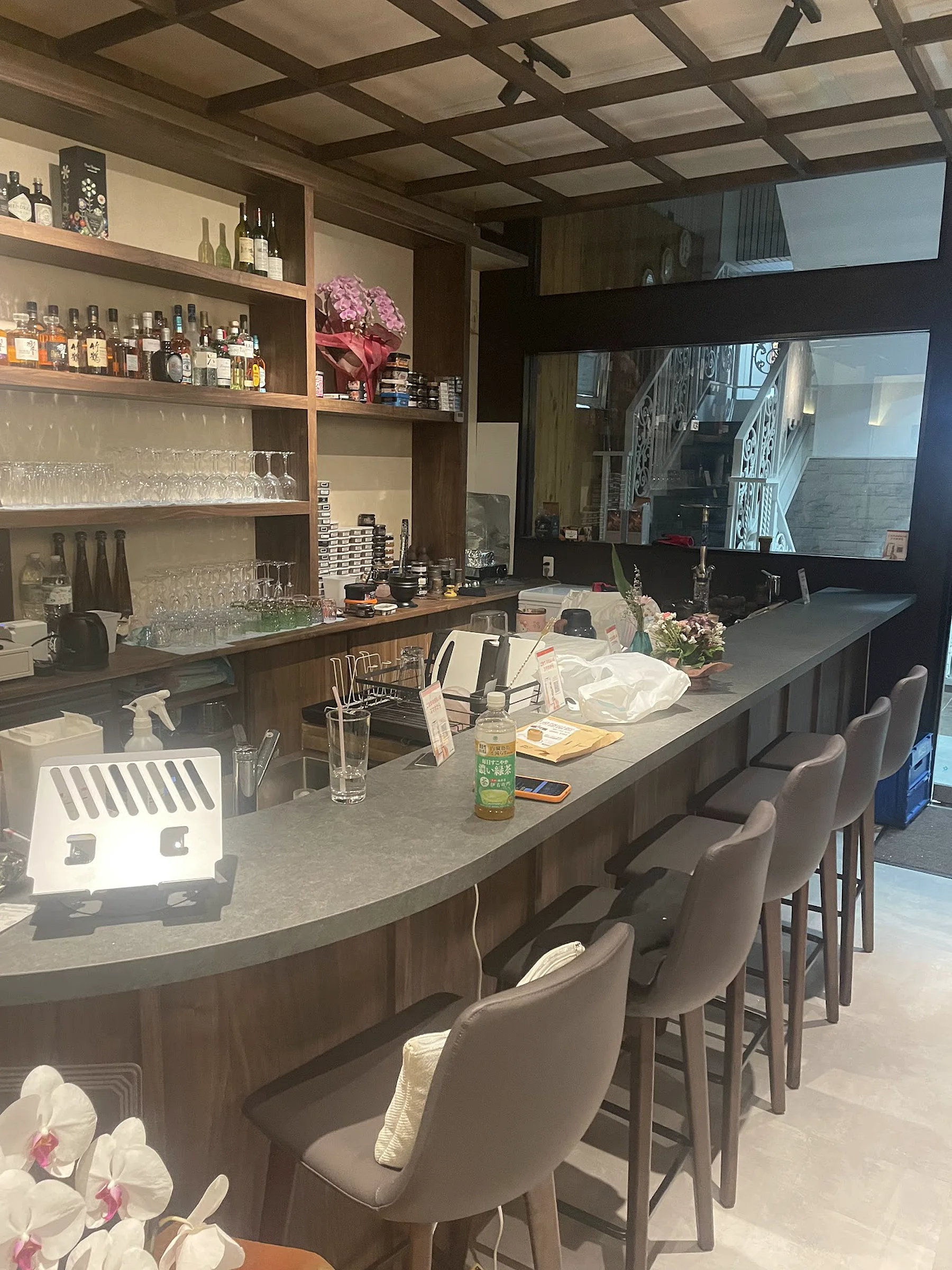 Backlit glassware on dark walnut shelves behind a bare stone counter, under a coffered wooden-lattice ceiling